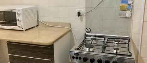 A kitchen with a white tiled backsplash, a white toaster oven, a stainless steel gas stove, and a wooden drawer unit.