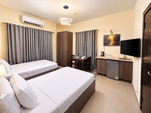 A hotel room with two beds, a desk, a television, and a kitchenette. - Sakan 275 (New Cairo)