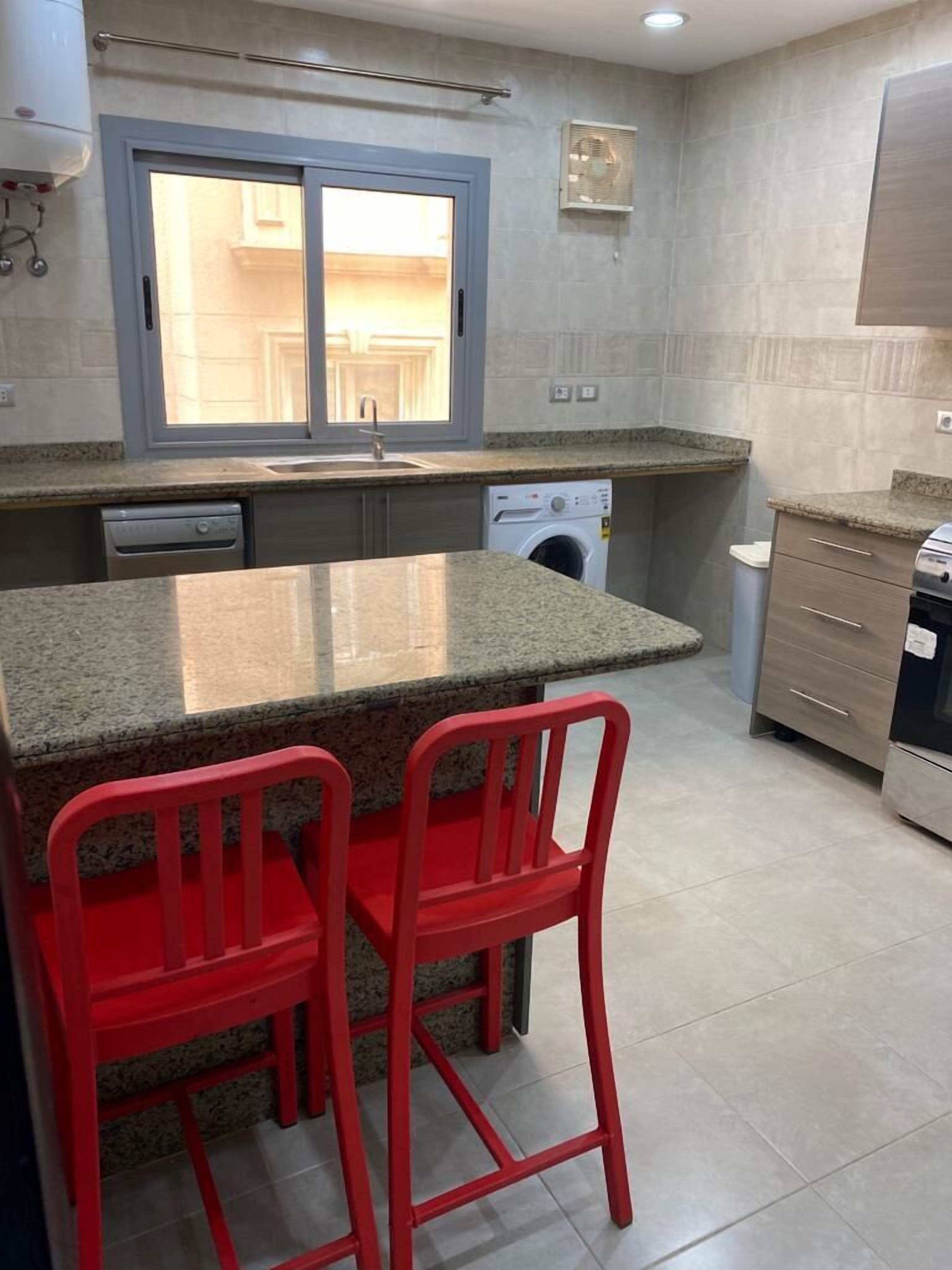 A kitchen with granite countertops, a built-in washing machine, and red bar stools.