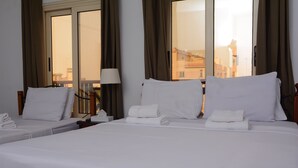 Ein Hotelzimmer mit einem großen Bett, zwei Nachttischen, einer Lampe und Blick auf die Stadt durch das Fenster.