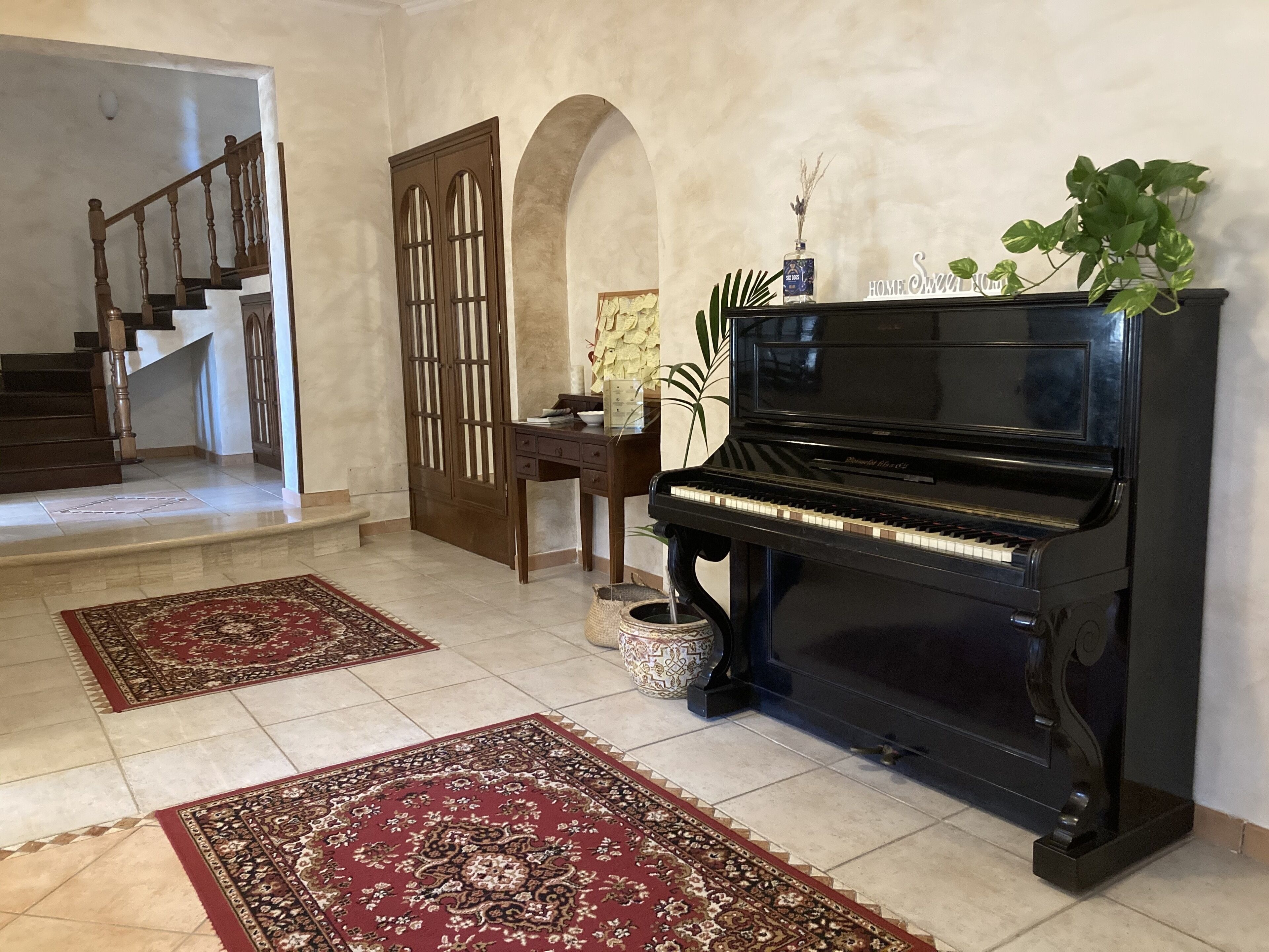 A spacious living area with a grand piano, a staircase, and a decorative archway.
