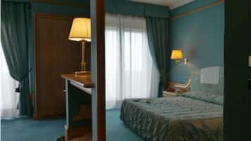A hotel room with a bed, a desk, a chair, and a lamp.