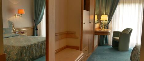A hotel room with a bed, a bedside table, a chair, a desk with a lamp, and a mirror.