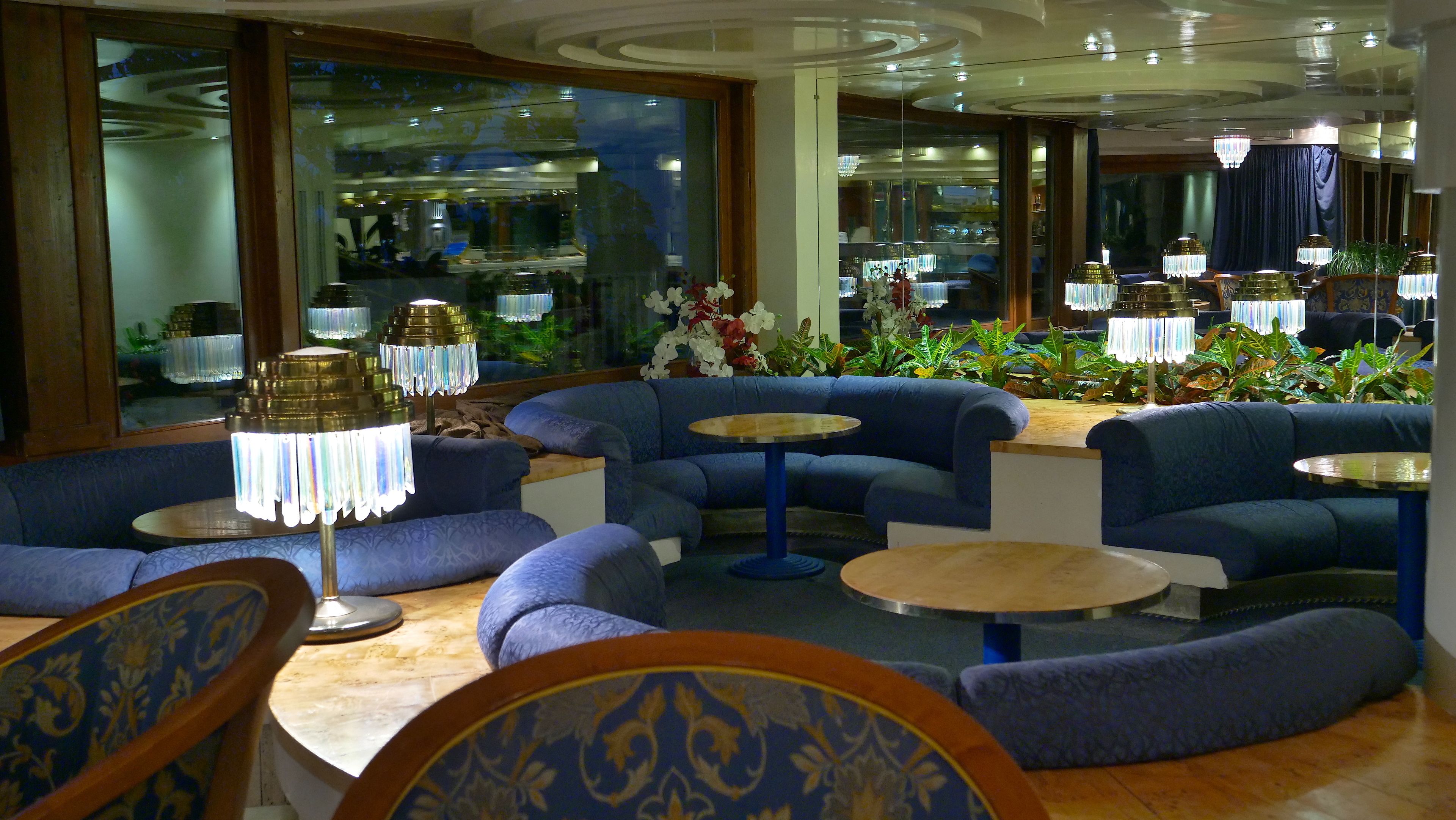 Ein stilvoller Lounge-Bereich mit blauen Polster-Sofas, runden Holztischen und dekorativen Lampen.