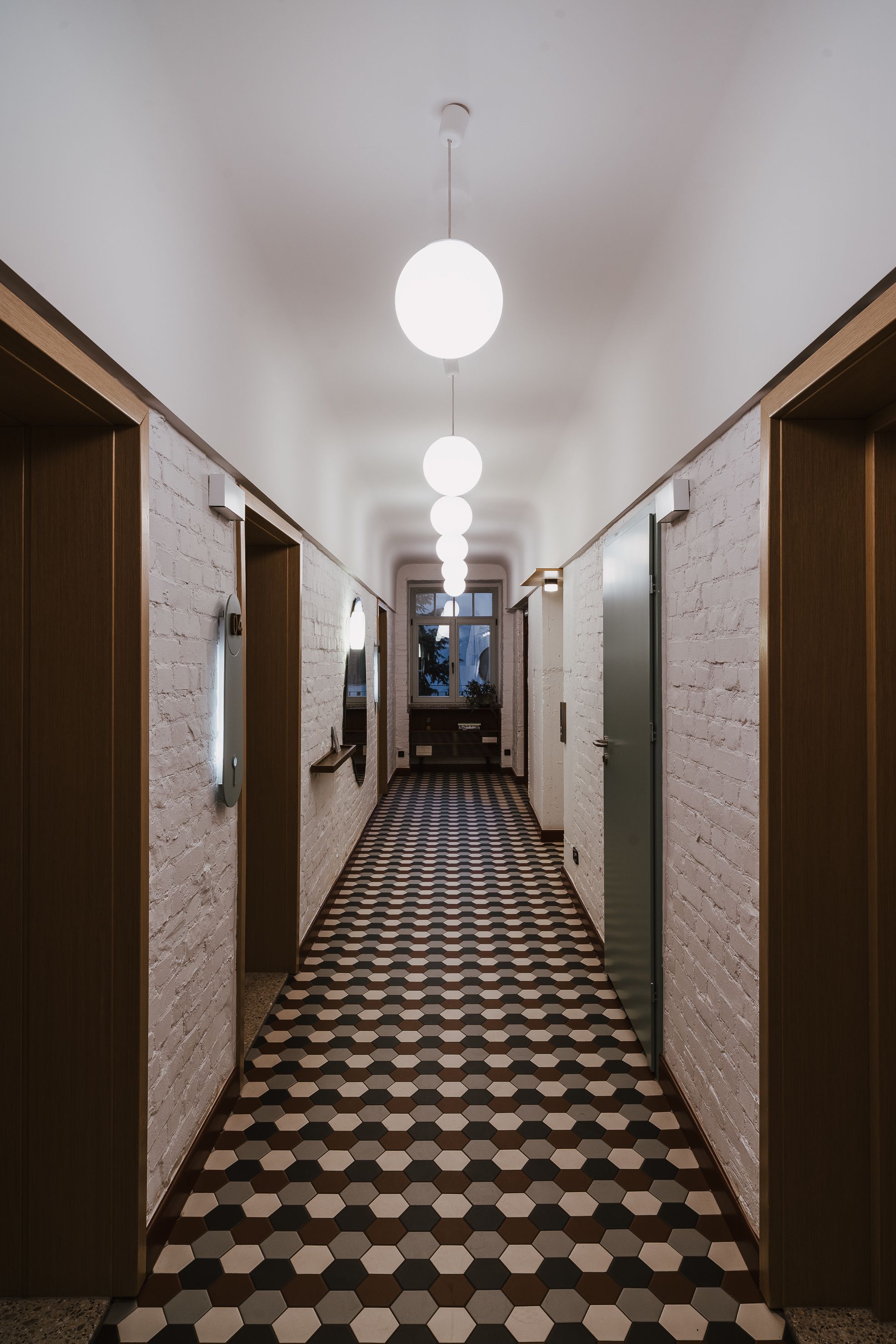 Un couloir doté d’un sol à motifs, de portes en bois et de luminaires suspendus.