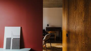 A room with a red wall, a wooden door, a white framed picture, a wooden chair, and a desk with a television.