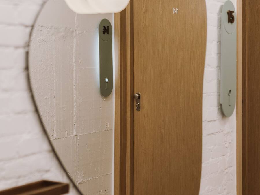 Un pasillo con un espejo redondo que refleja una puerta, una lámpara y una placa con un número.