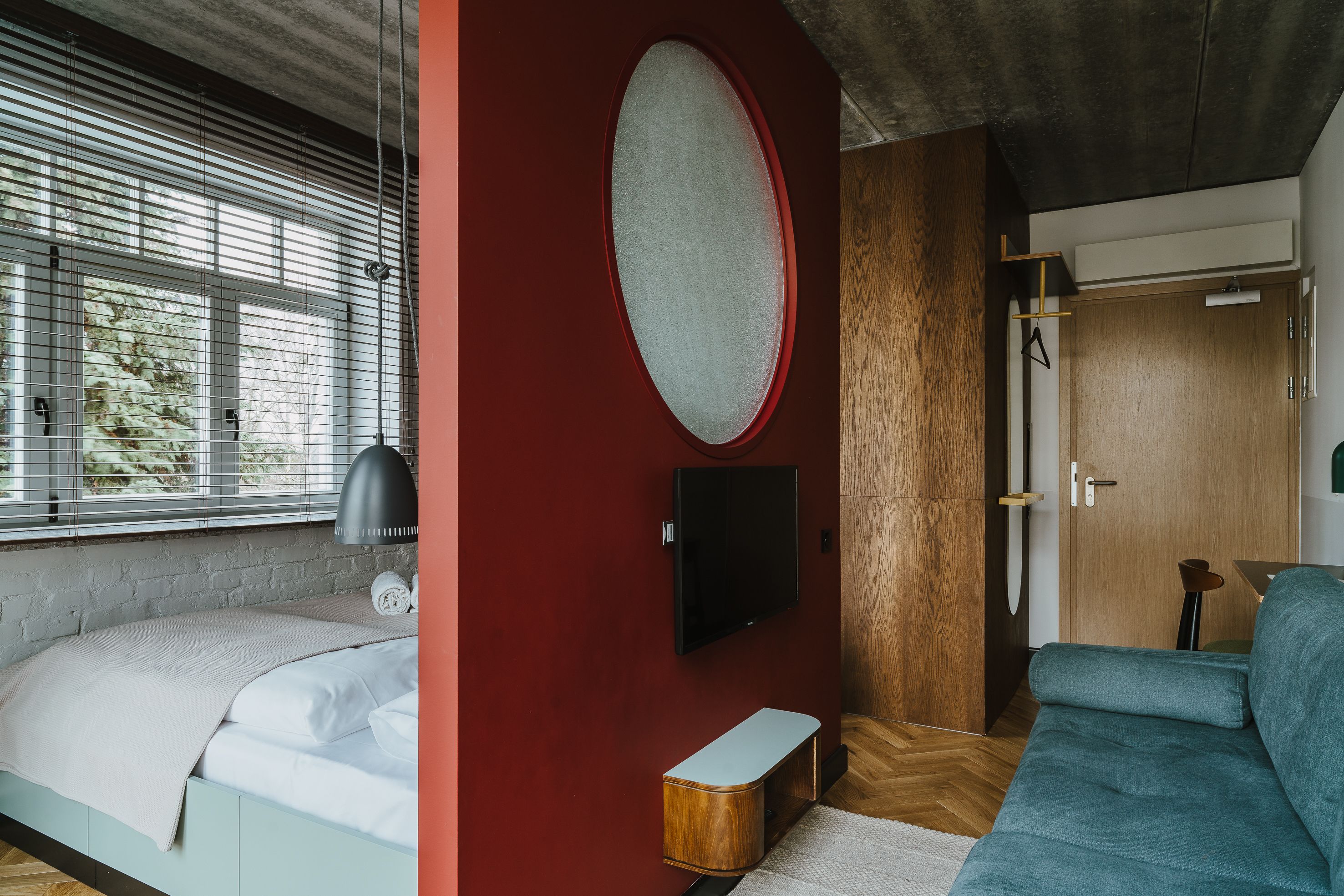 Un dormitorio moderno con cama, televisor, pared roja y puerta de madera.