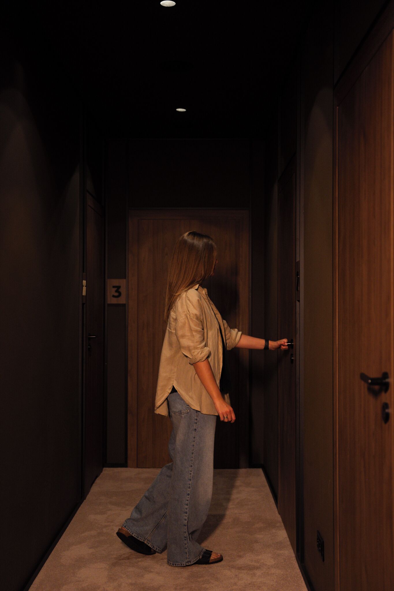 Une personne se trouve dans un couloir, devant une porte portant le numéro « 3 ».