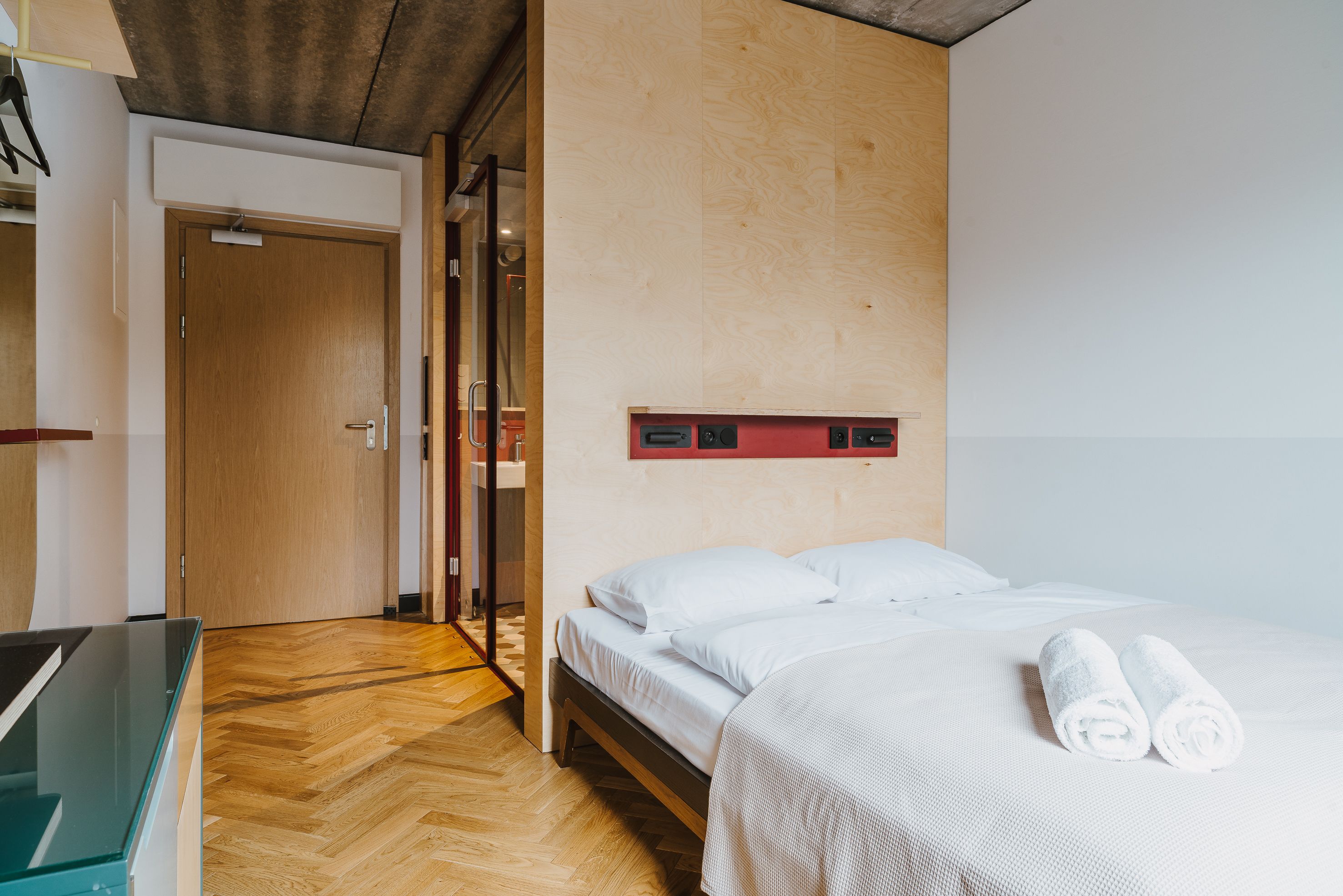 Una habitación de hotel con suelo de madera, una cama con ropa de cama blanca y una mesa de vidrio.
