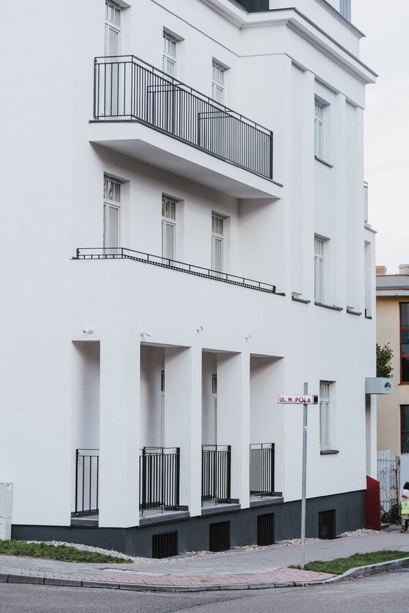 Un edificio de varios pisos con balcones, un letrero que dice "UL. W. POŁA" y un sendero para peatones.