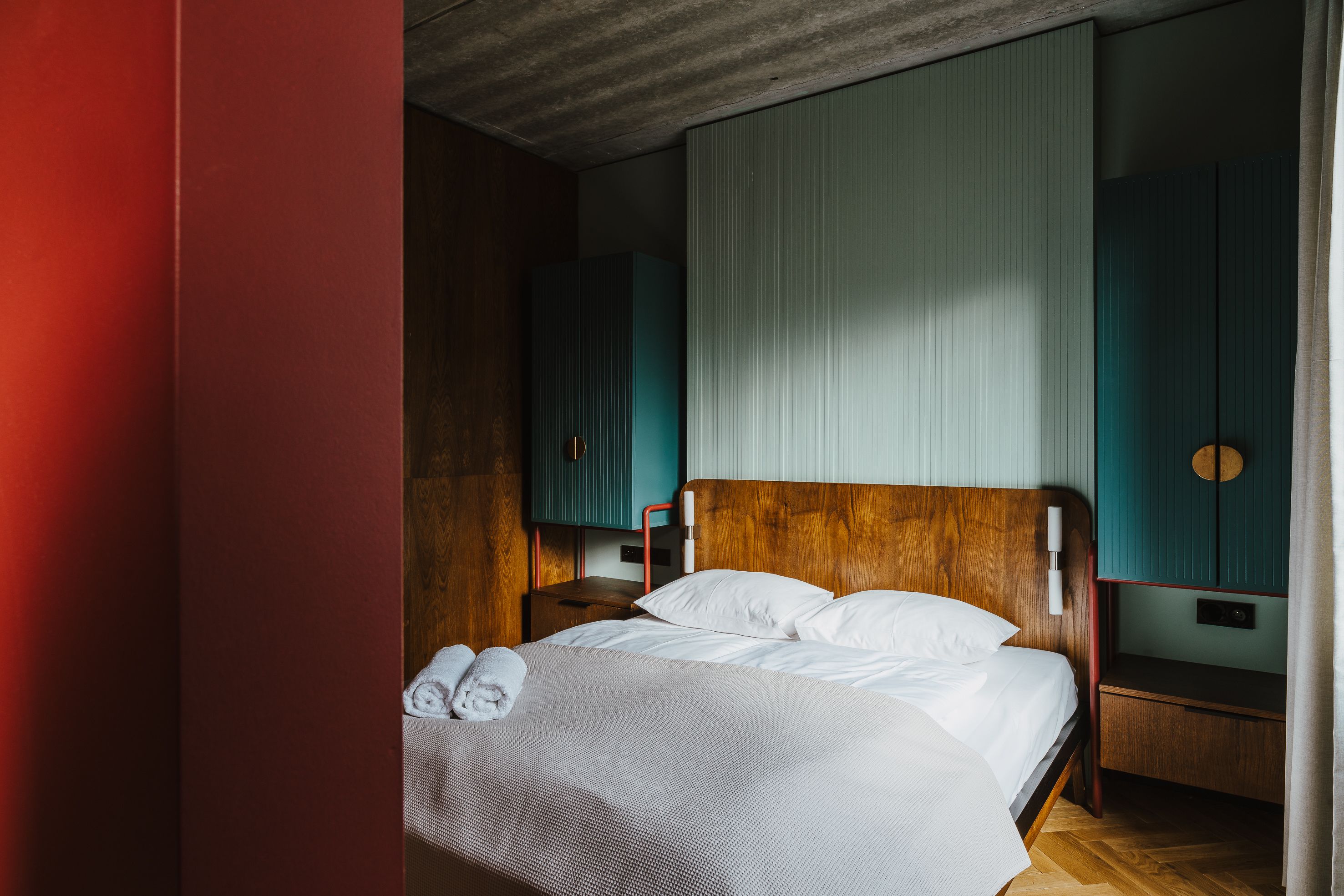 Uma cama bem arrumada com lençóis brancos e toalhas dobradas, uma cabeceira de madeira e uma mesa de cabeceira com abajur.