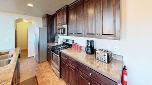 Una cocina con gabinetes de madera oscura, electrodomésticos de acero inoxidable, encimera de granito y extintor.