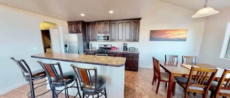 Una cocina moderna con armarios de madera oscura, una isla central con taburetes y un comedor con sillas de madera.