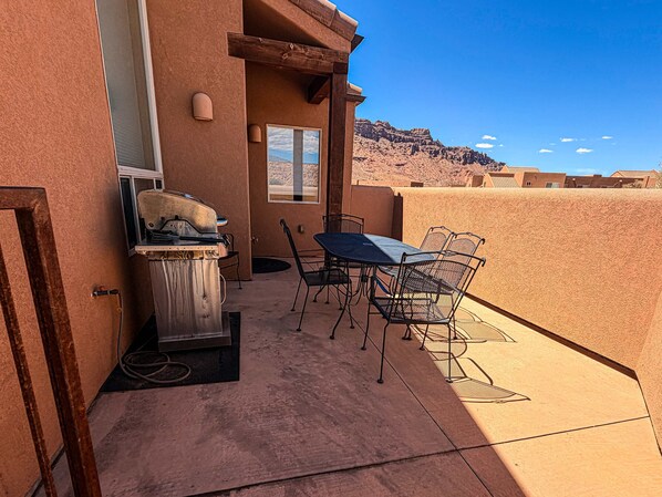 Un patio exterior con una parrilla, una mesa y sillas, con vistas a un paisaje desértico.