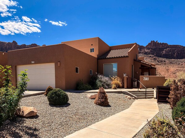 A modern two-story house with a garage, a covered patio, and a mountain backdrop.