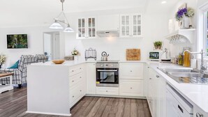 Eine moderne Küche mit weißen Schränken, einem Einbauofen, einer Spüle und einem Essbereich mit einer Couch und einem Tisch.