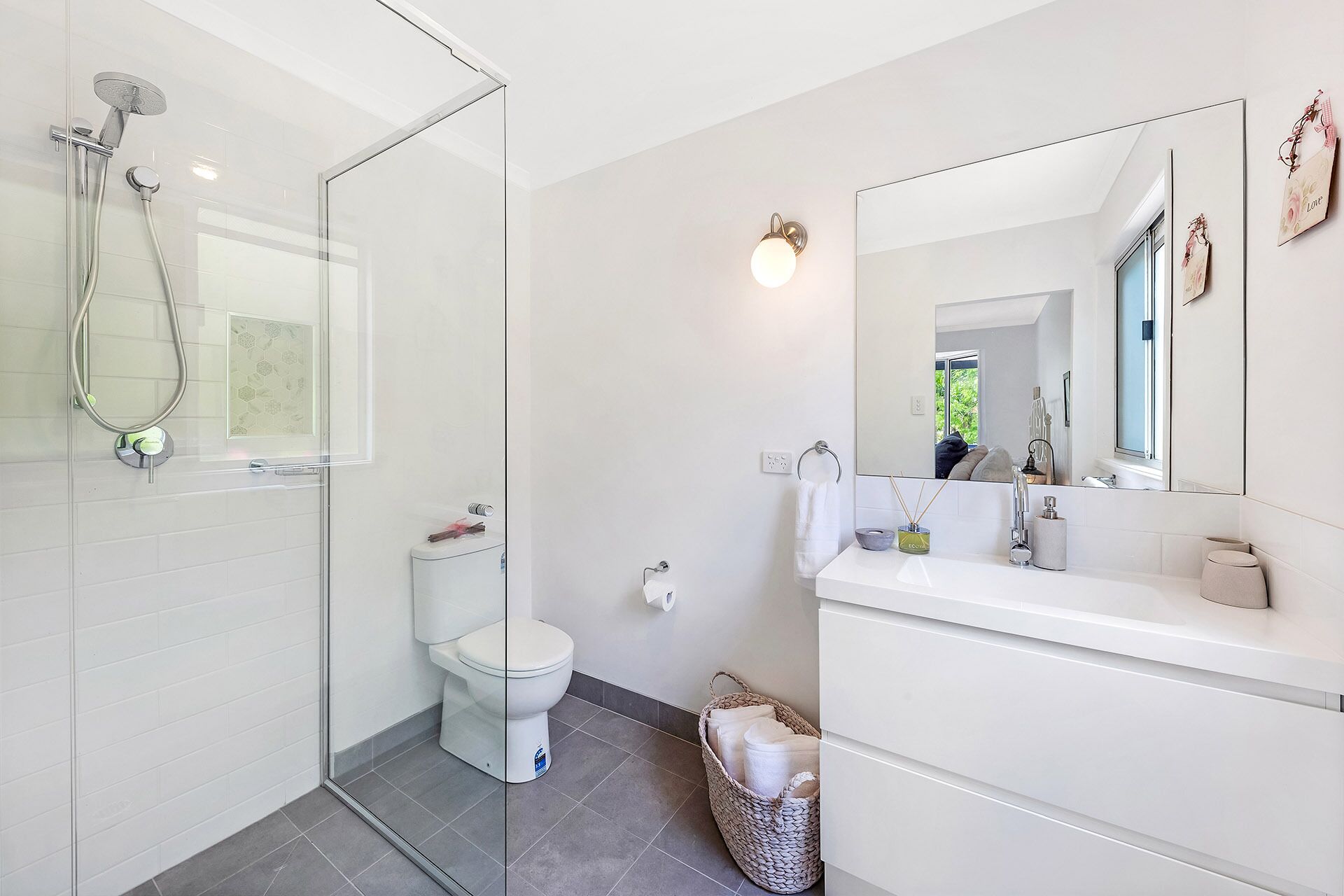 Ein modernes Badezimmer mit Duschkabine aus Glas, Toilette, Waschbecken mit Spiegel und einem Wäschekorb mit Handtüchern.