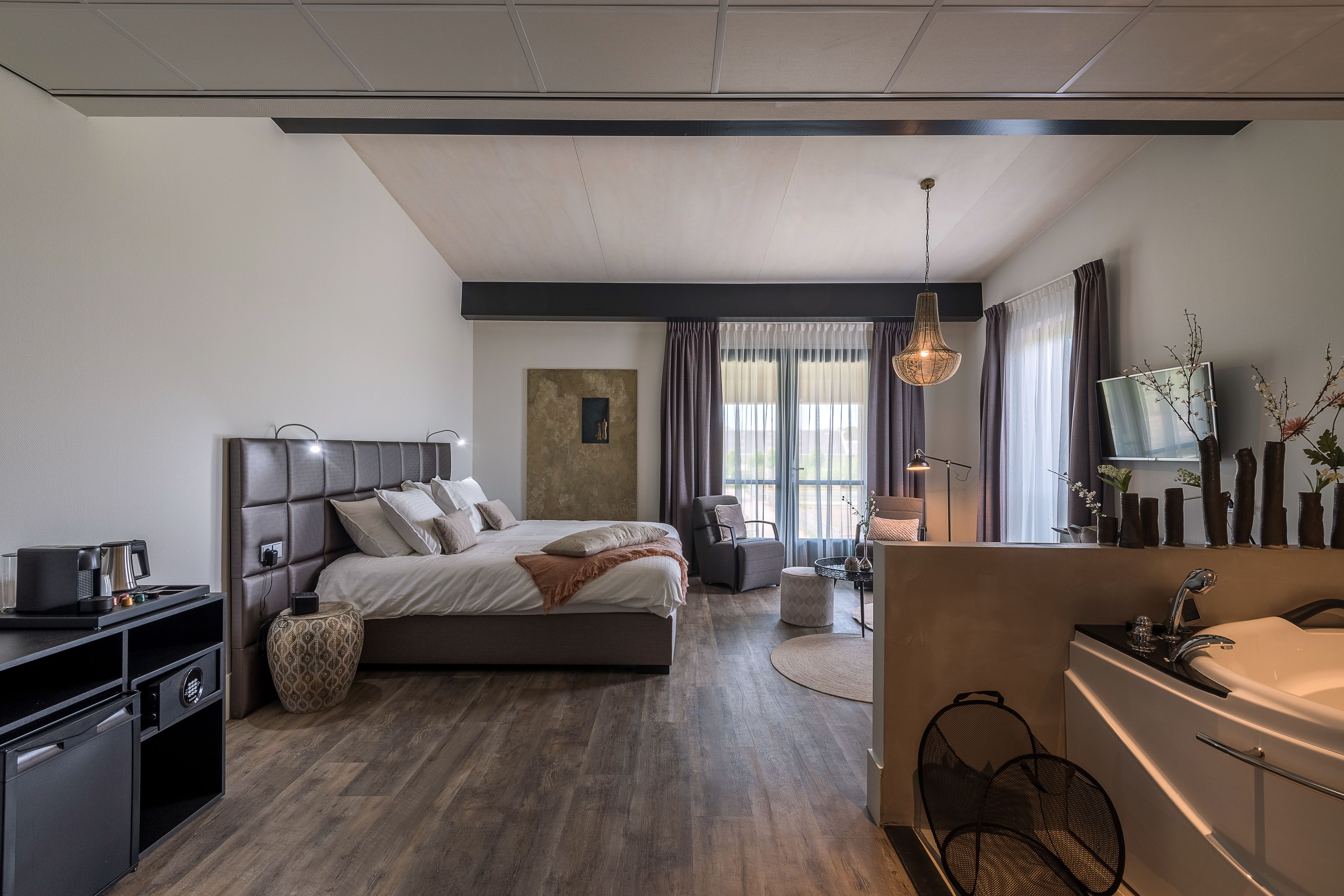 Quarto moderno com uma cama grande, mesas de cabeceira, uma escrivaninha e um banheiro com pia e espelho.