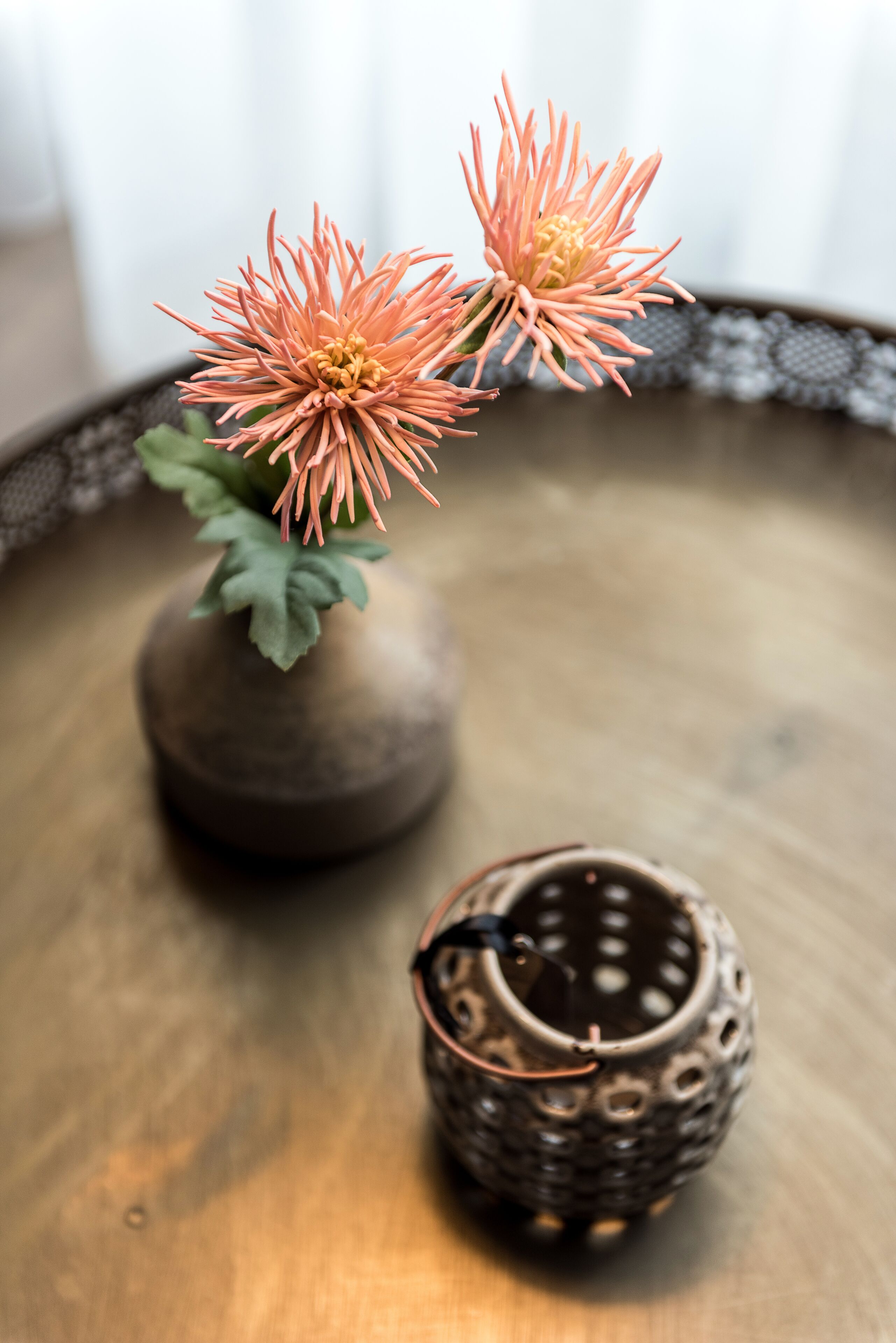 Un petit pot en céramique, rond, de couleur foncée, avec une surface texturée, et à côté, sur une surface en bois, un petit récipient en céramique ouvert et perforé.