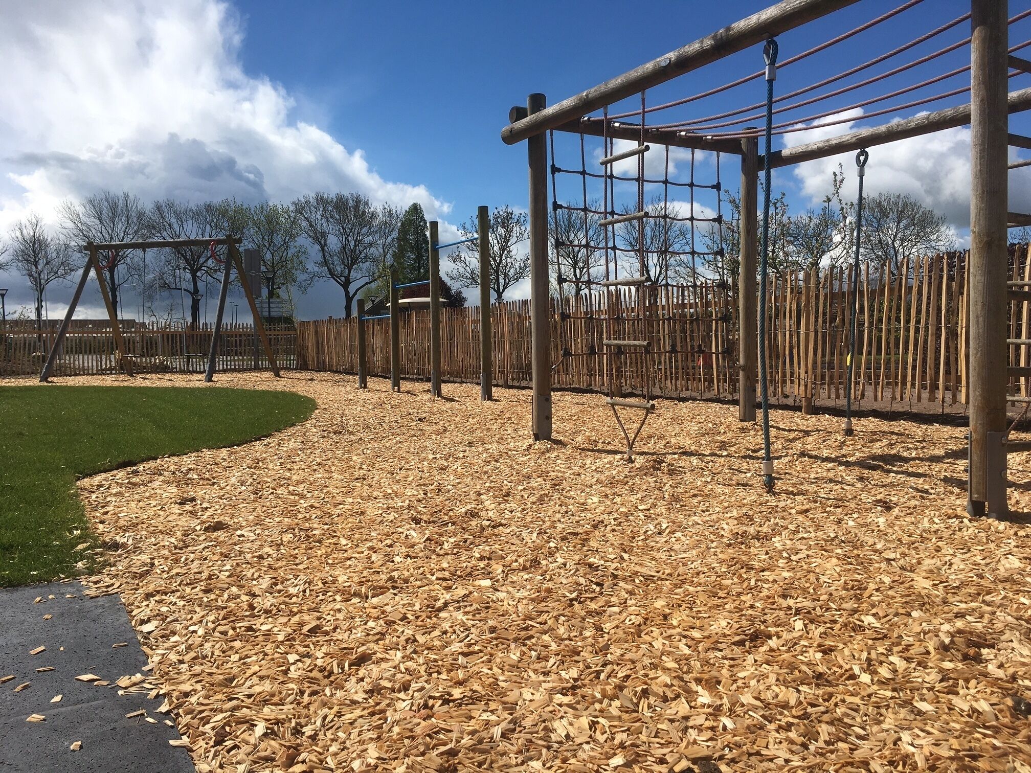 Uma área de recreação infantil com um brinquedo de madeira, cobertura de solo com lascas de madeira e um cercado.