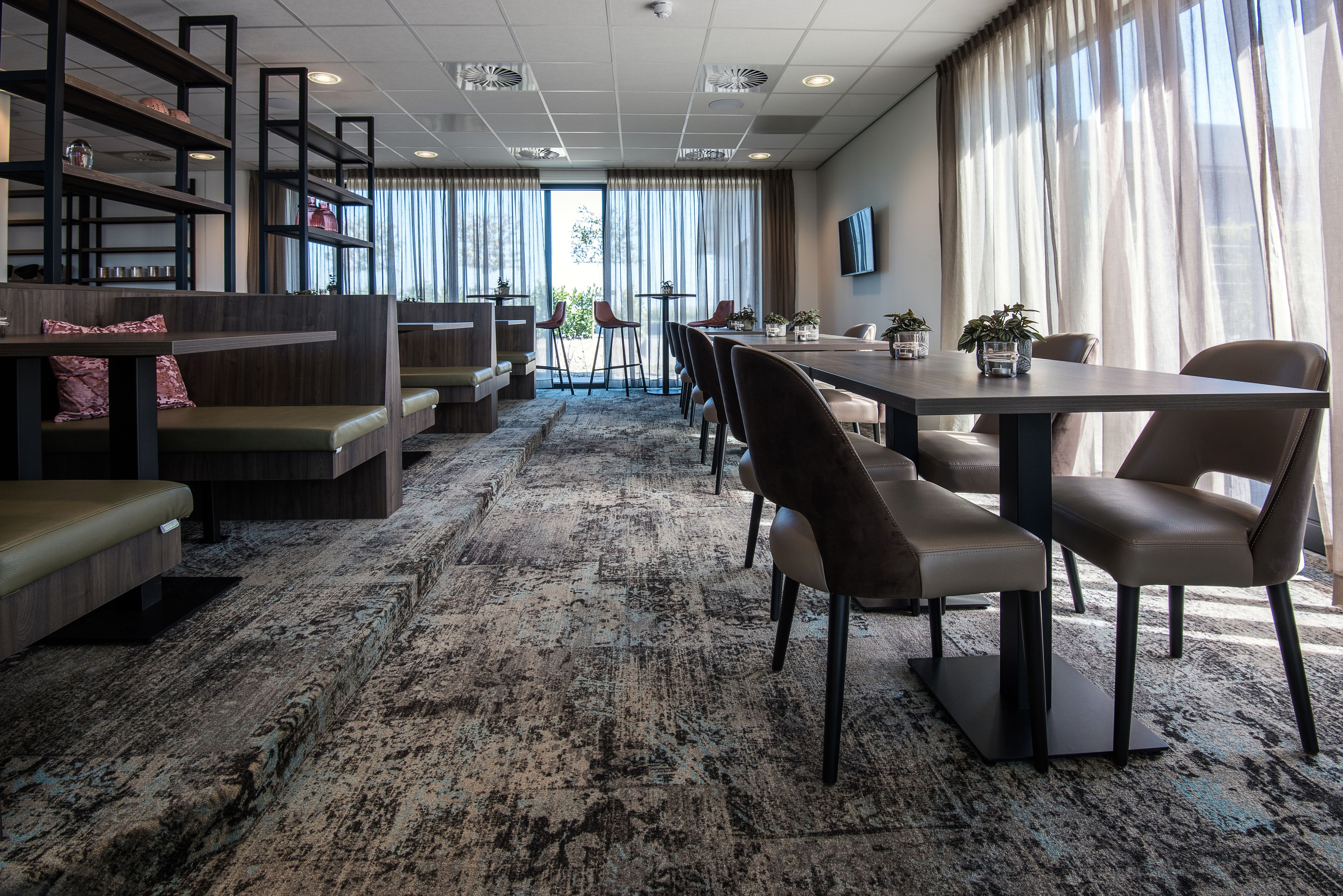 Eine moderne Hotelhalle mit einer langen Rezeption, Sitzgelegenheiten und großen Fenstern mit Vorhängen.