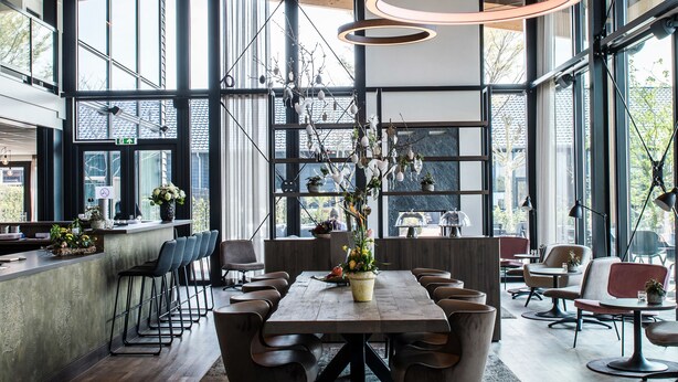 Un interior moderno con una amplia mesa de comedor, múltiples sillas y un arreglo floral central.