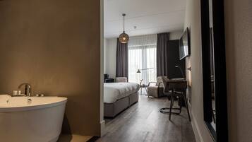 Quarto de hotel moderno com uma banheira grande, uma cama, uma escrivaninha e uma televisão.