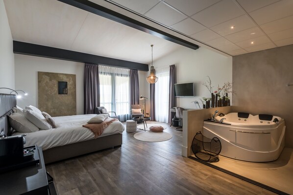 Un dormitorio moderno con una cama grande, una sala de estar, un escritorio, un televisor y un jacuzzi.