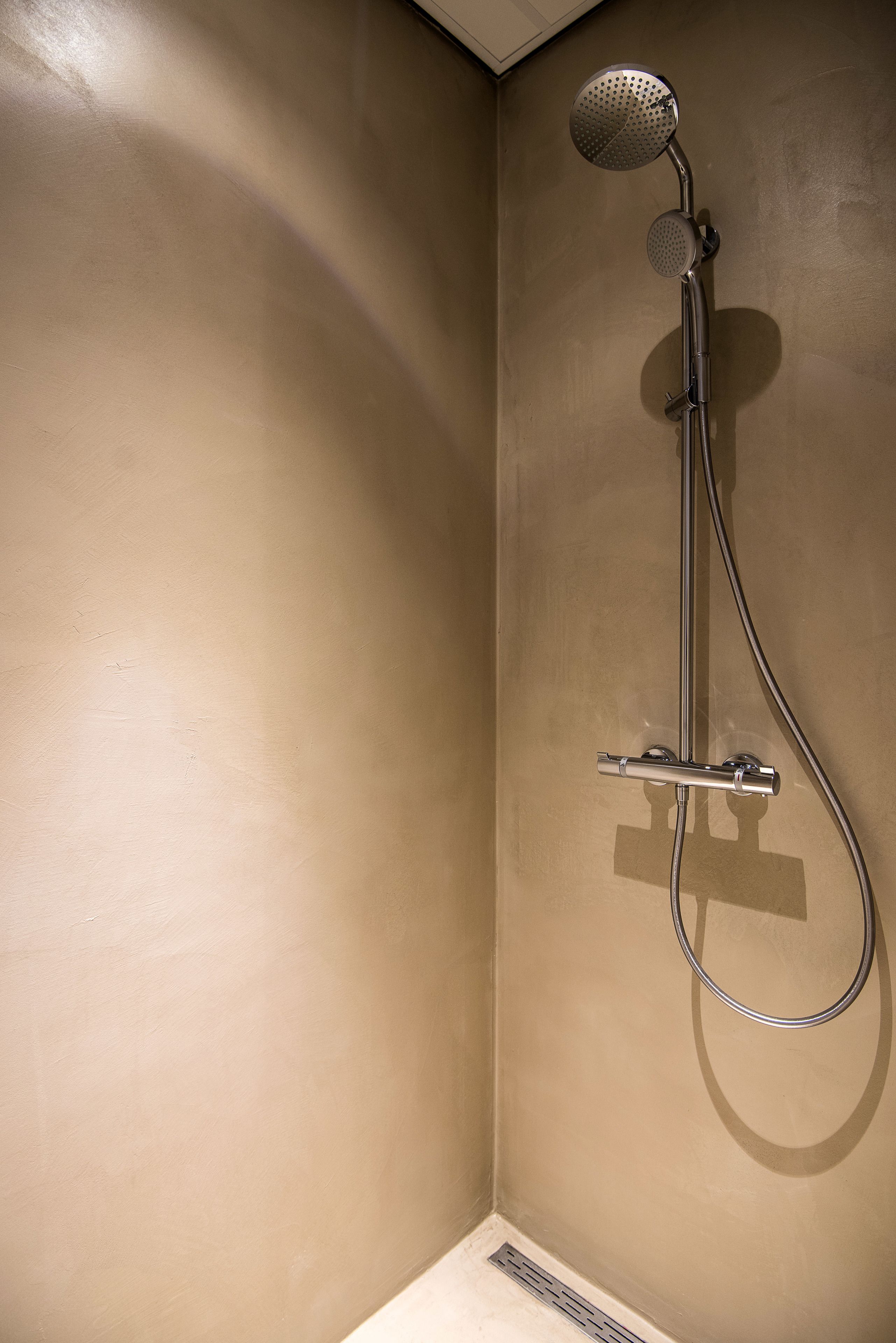 A shower with a handheld showerhead and a wall-mounted control panel.