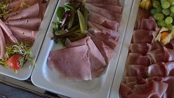 Un bufé con diversos alimentos, incluyendo carnes en rodajas, frutas y verduras.