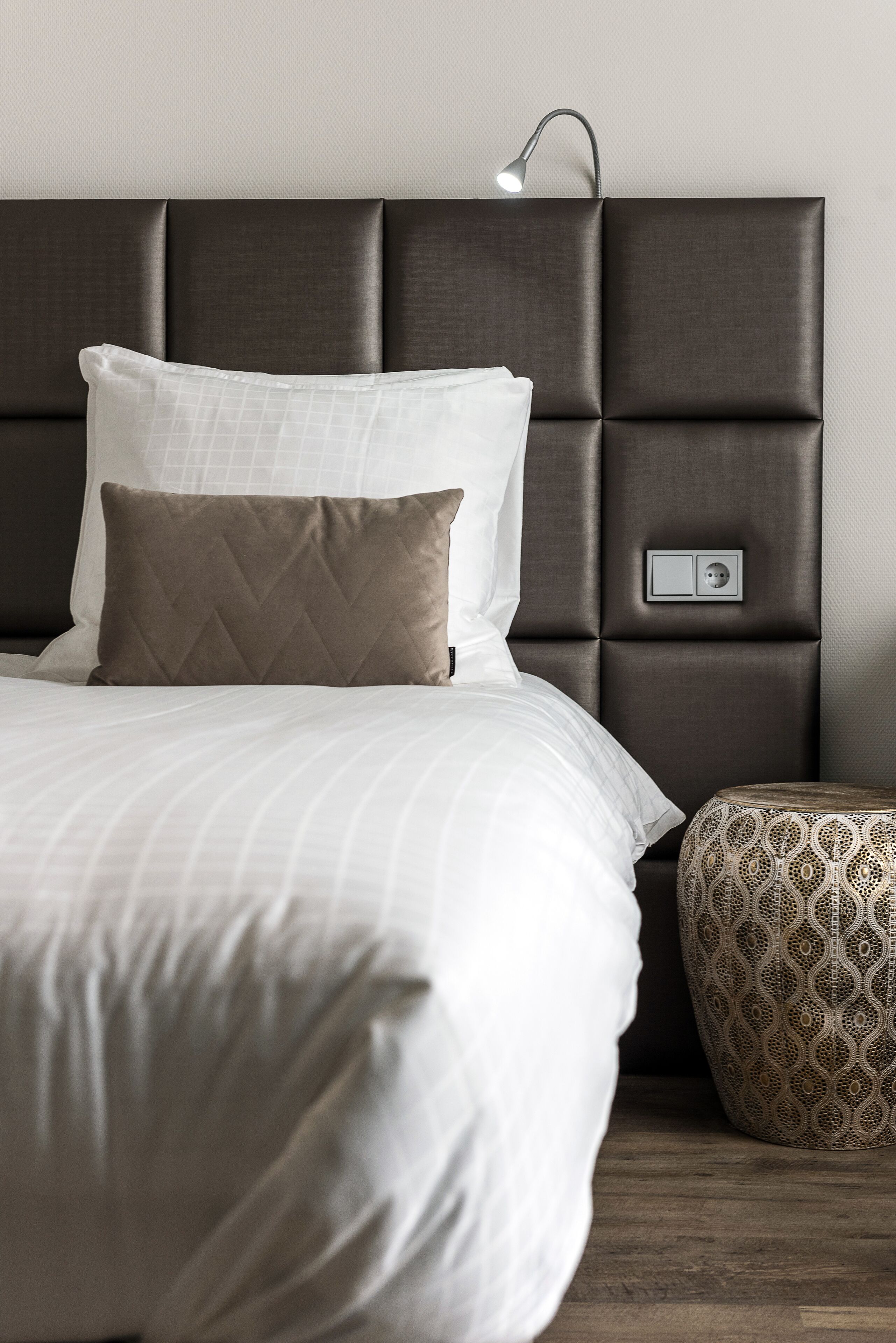 Una cama bien hecha con cabecera, lámpara de noche y reposapiés estampado.