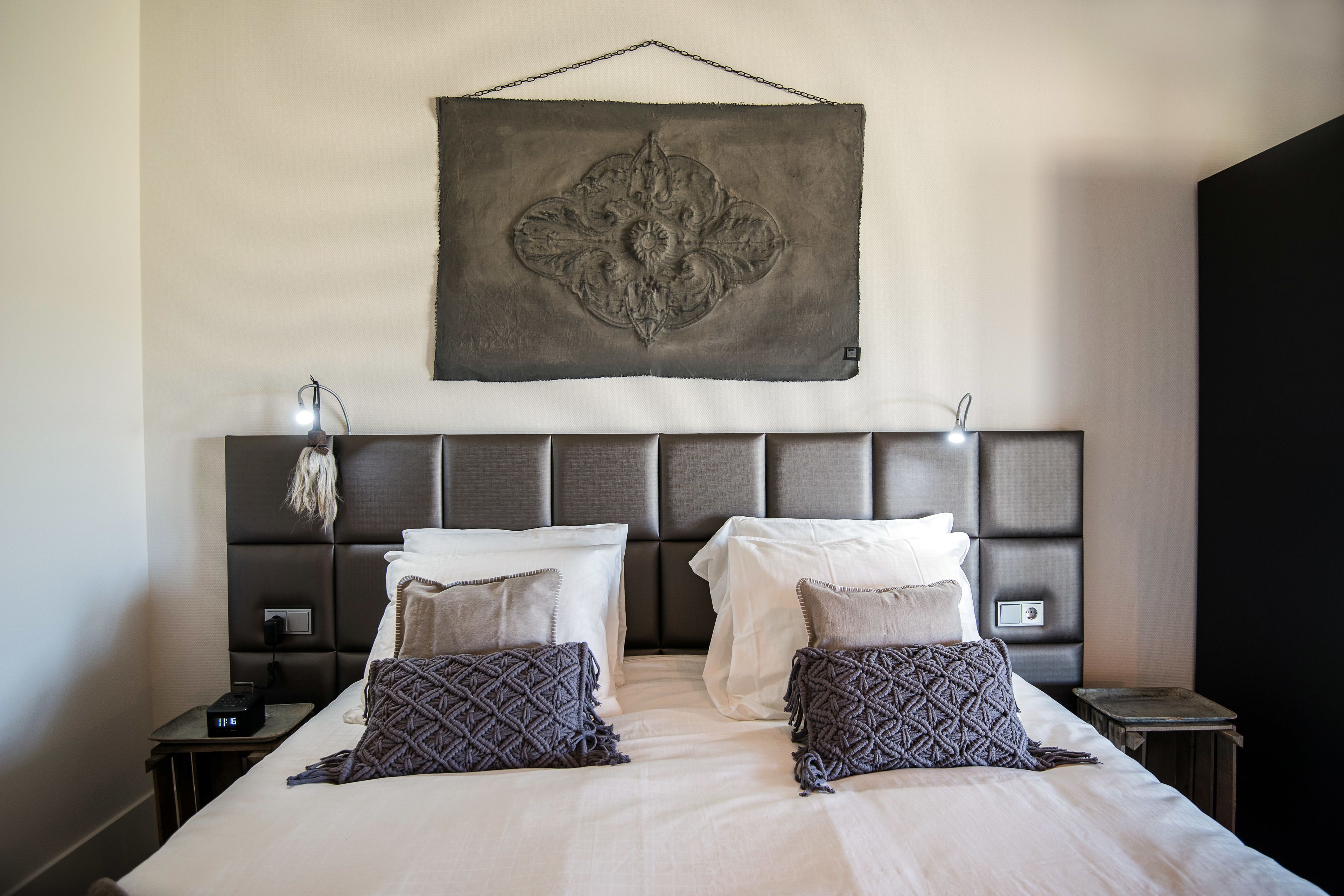 A double bed with two pillows, a bedside table with a lamp, and a wall-mounted artwork above the bed.