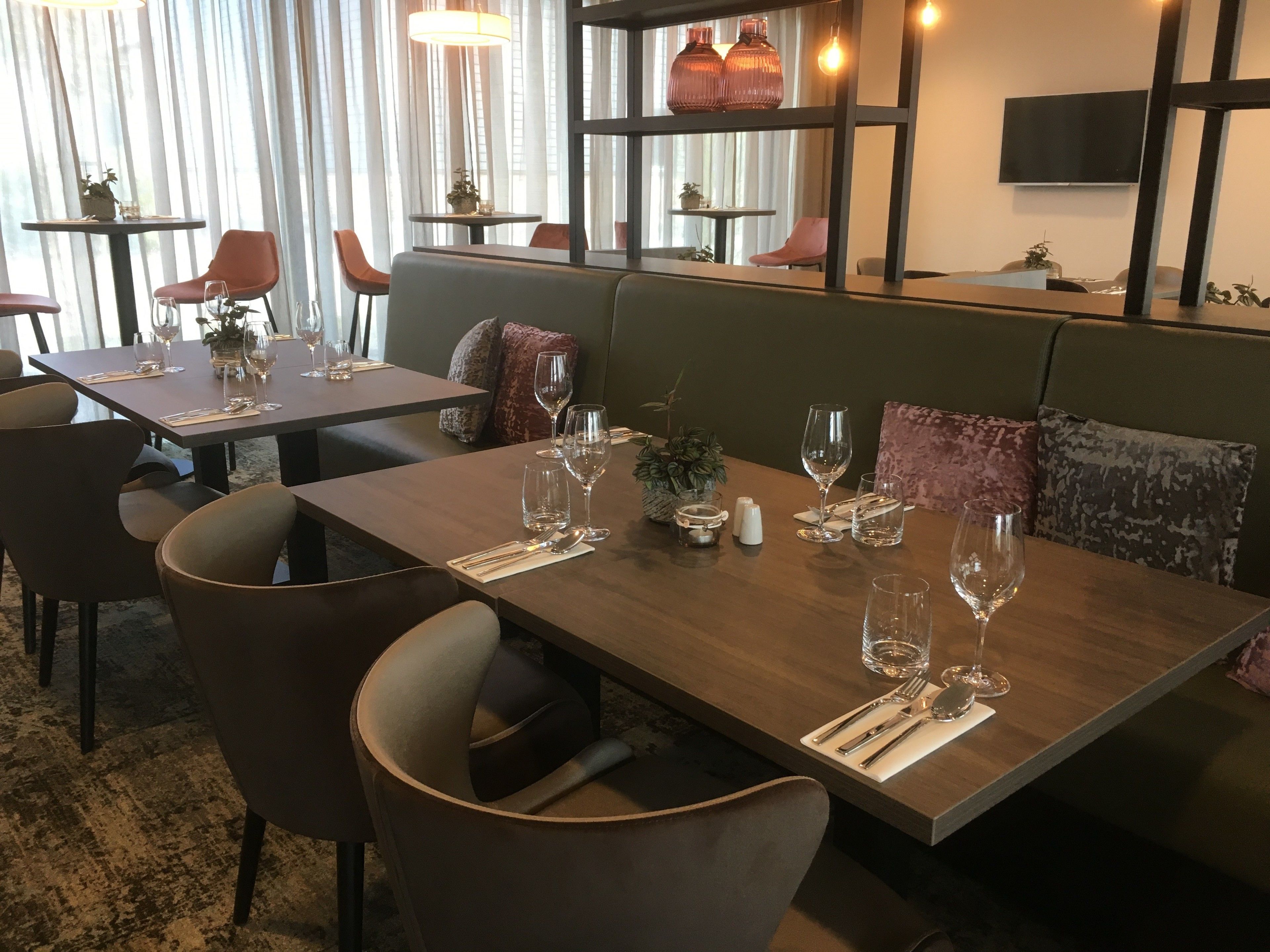 Un restaurant avec des tables en bois, des chaises rembourrées et un décor moderne comprenant un téléviseur et des lampes suspendues.