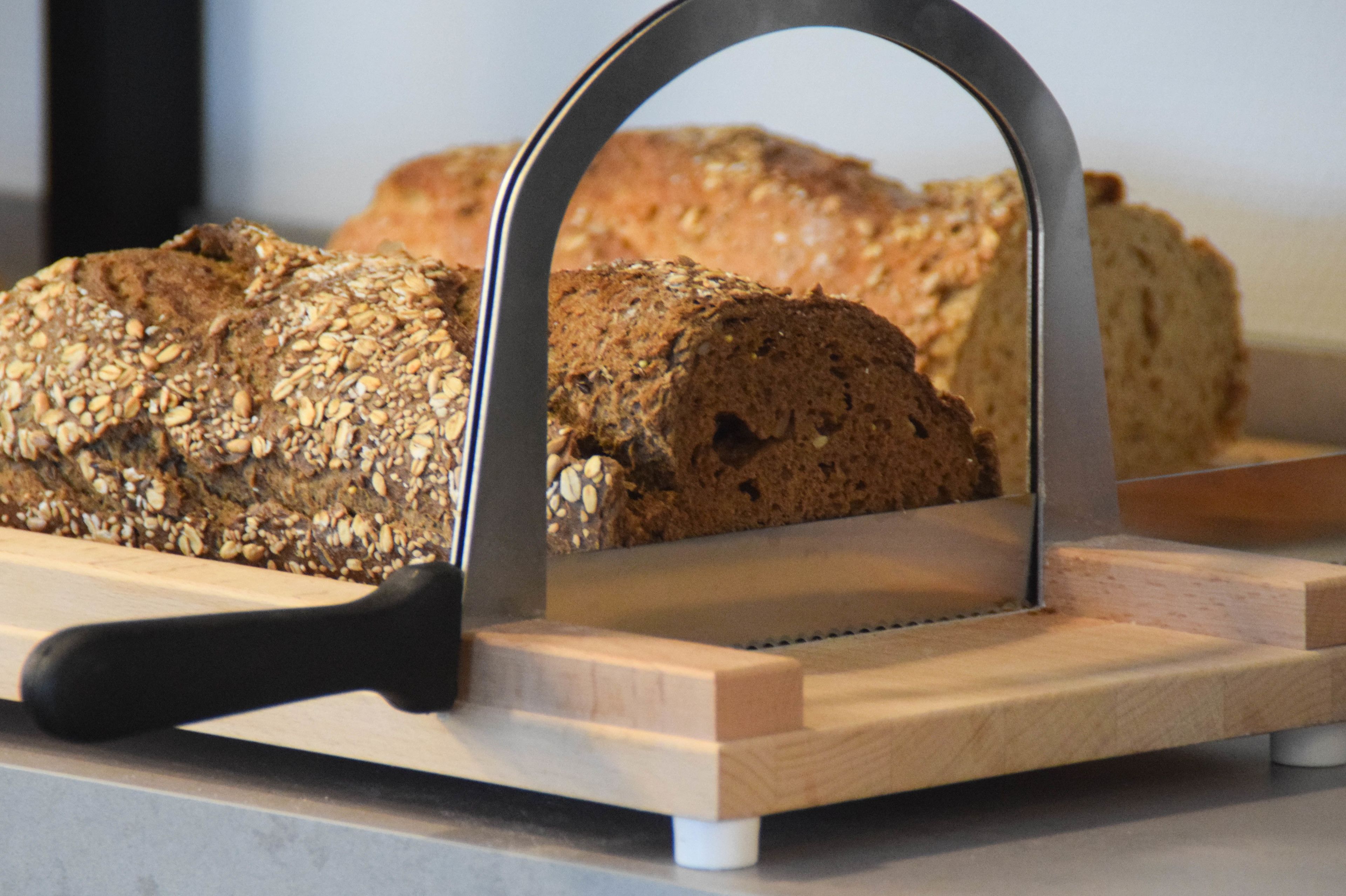 Een stuk volkorenbrood op een houten snijplank met een metalen broadsnijder.