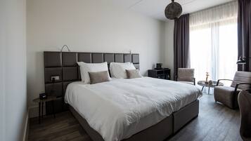 Una habitación de hotel moderna con una cama grande, una mesita de noche, una silla, una pequeña mesa redonda y un aplique colgante.