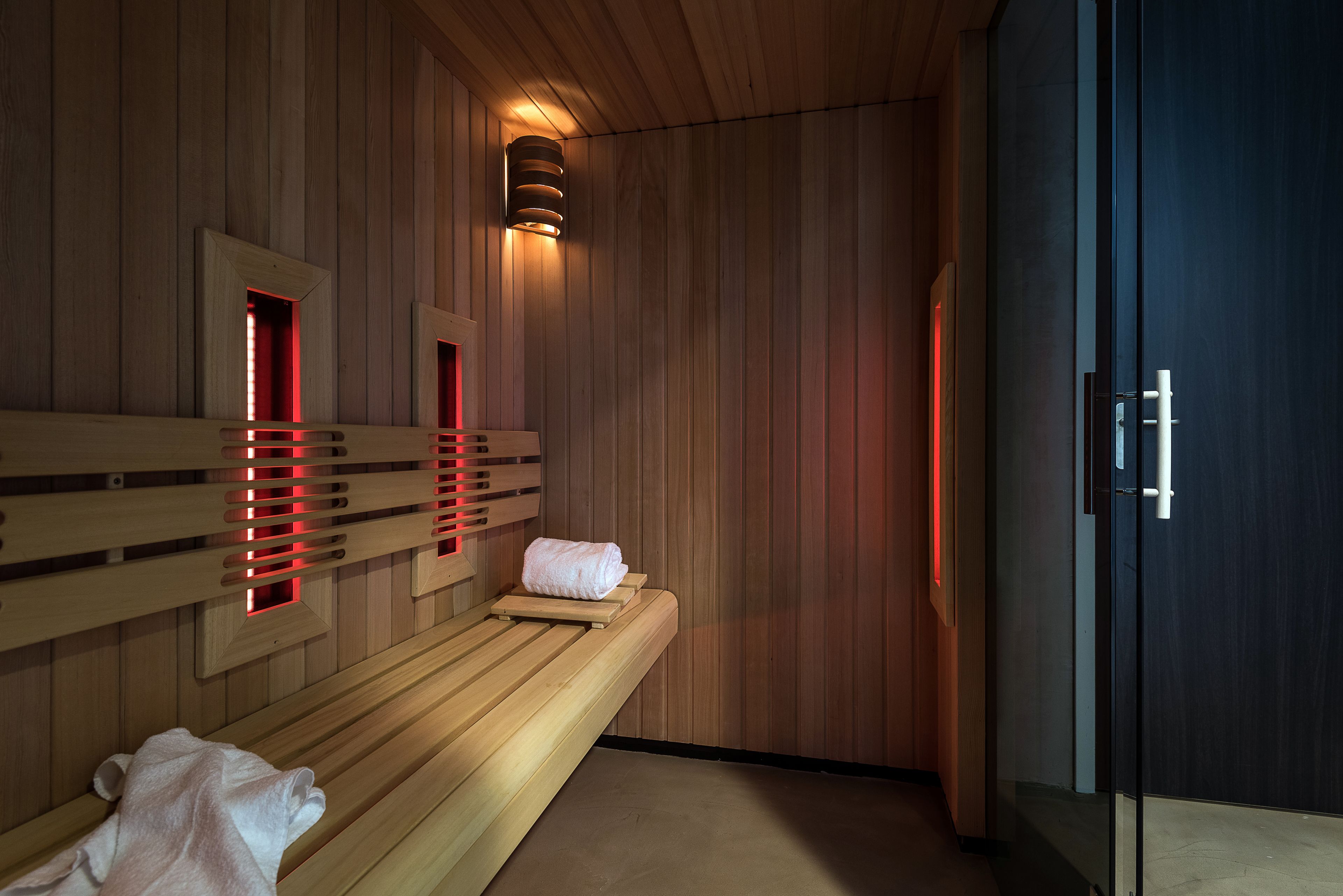 A sauna room with wooden benches, a glass door, and red lighting.