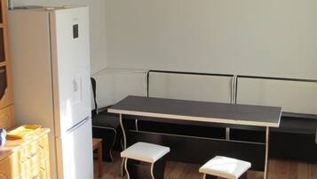 Une cuisine compacte avec un réfrigérateur blanc, un meuble en bois, un banc noir et une petite table accompagnée de deux tabourets.