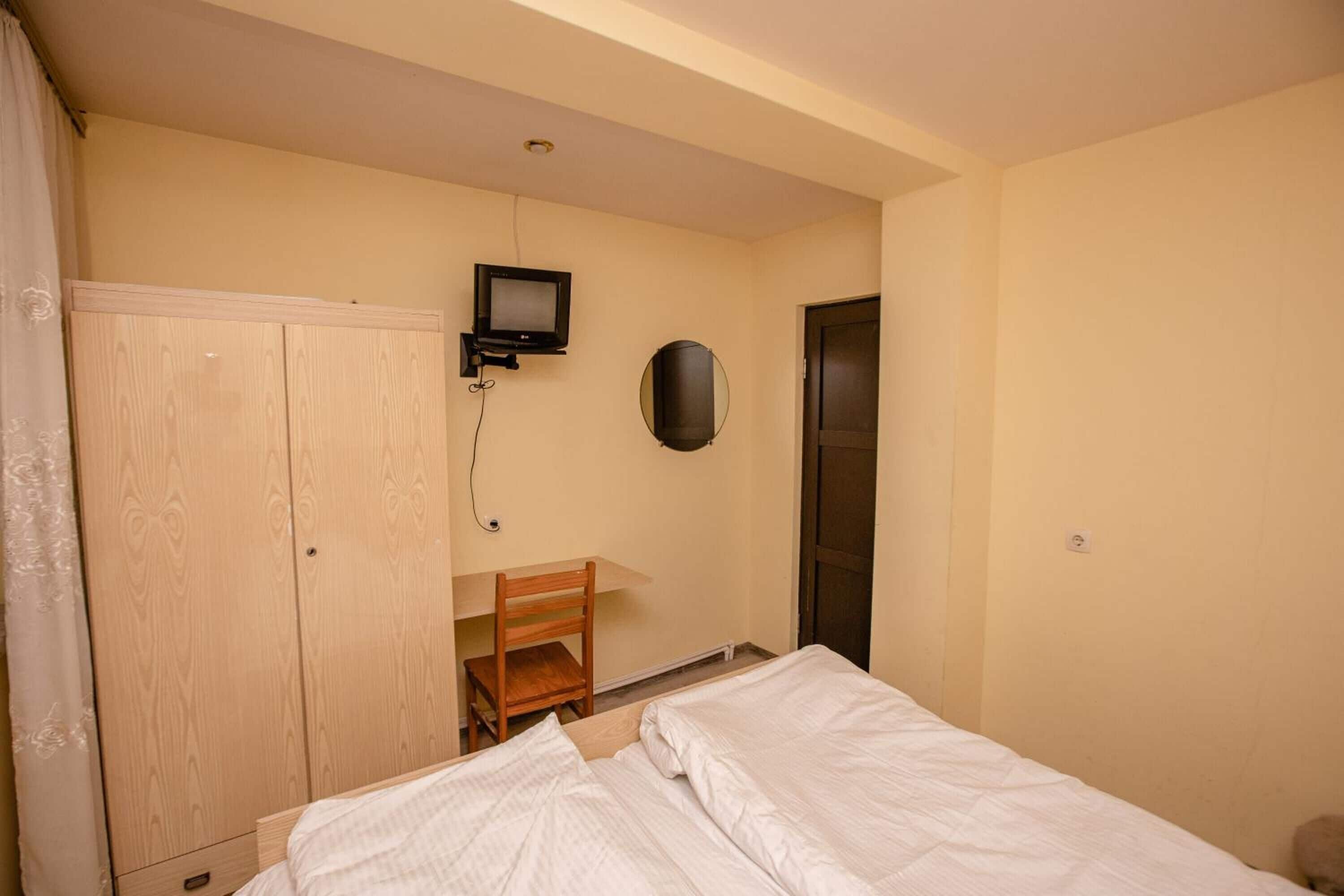 Une chambre à coucher comprenant un lit, un bureau avec une chaise, une armoire, un téléviseur et une porte.