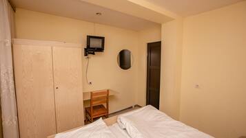 Une chambre à coucher comprenant un lit, un bureau avec une chaise, une armoire, un téléviseur et une porte.