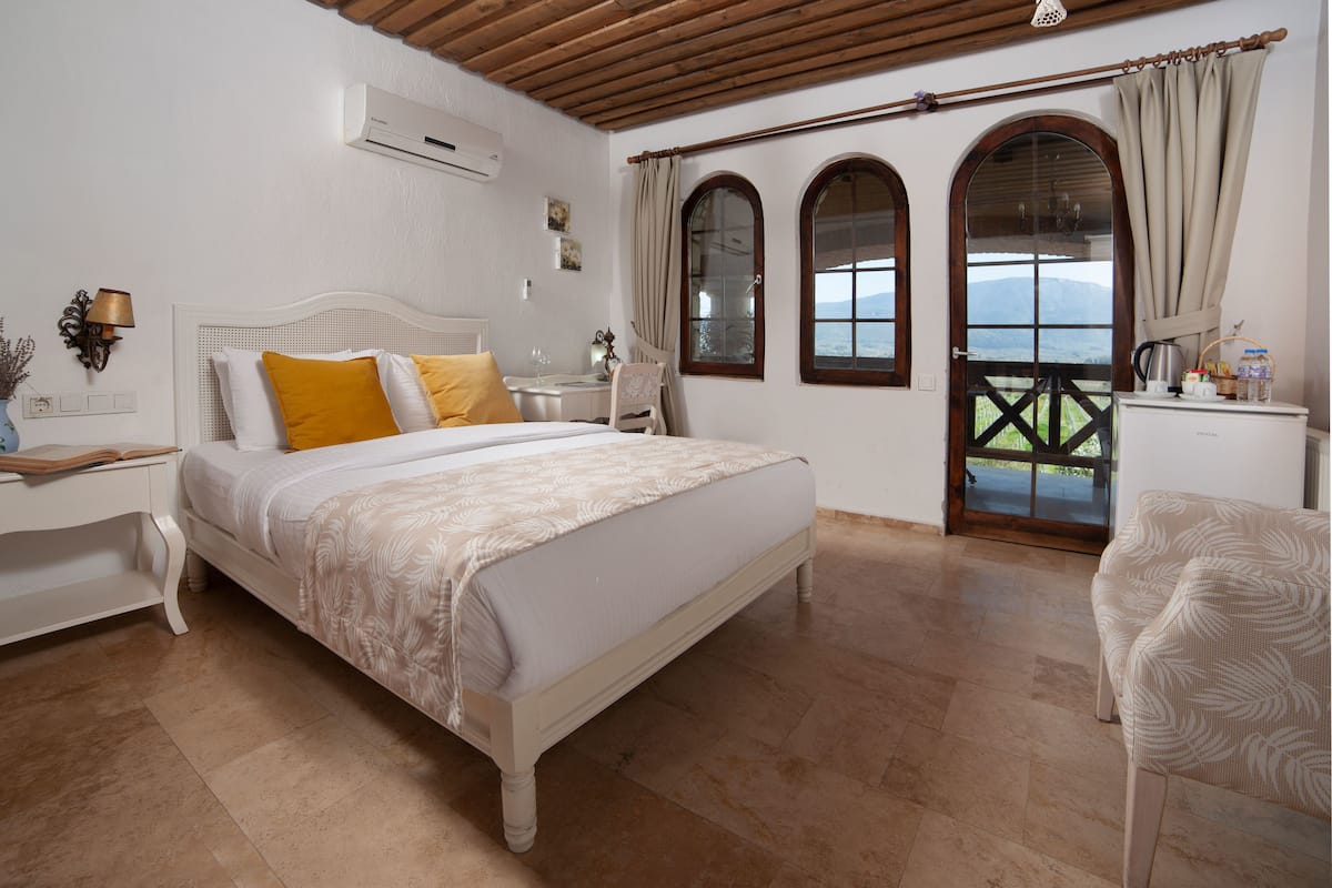 A bedroom with a bed, a nightstand, a chair, a desk, and a view through a door.