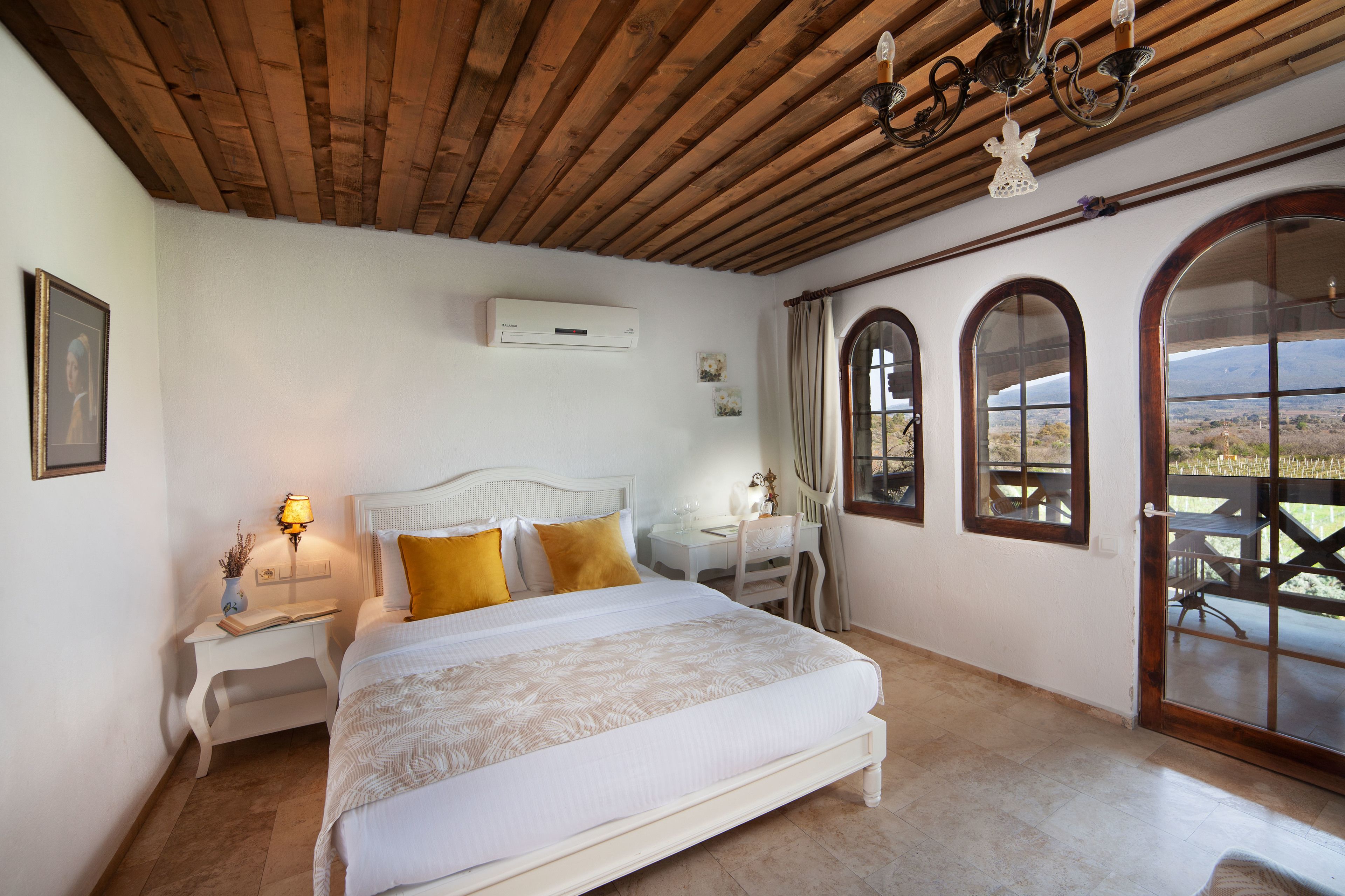 A bedroom with a bed, bedside tables, a desk, and a view through arched windows.