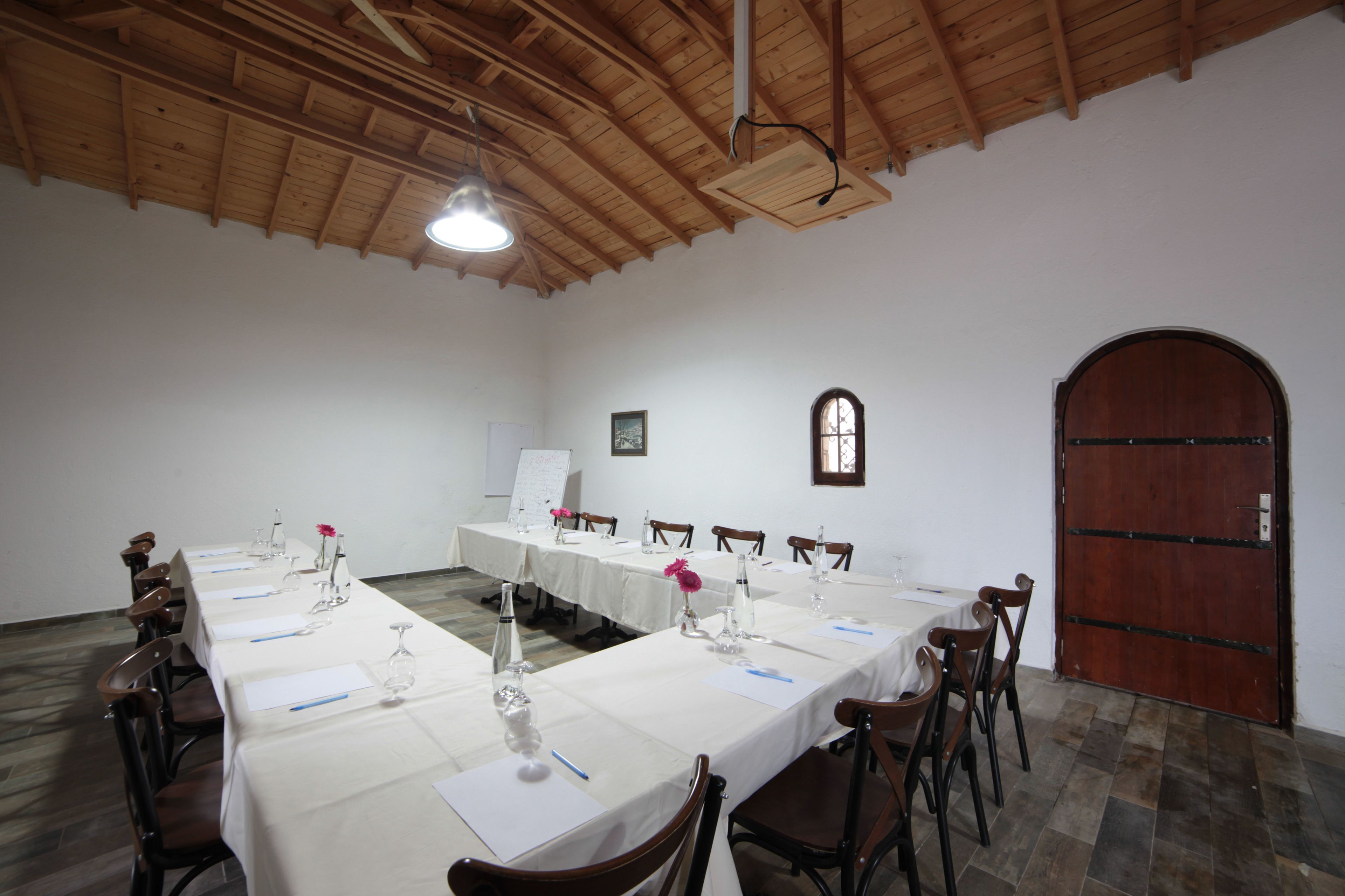 A conference room with long tables, chairs, a whiteboard, and a wooden door.