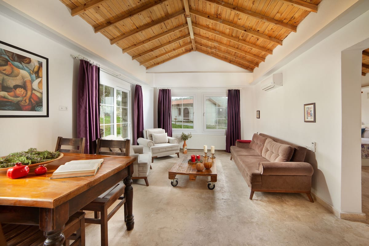 A spacious living room with a high wooden ceiling, a dining area with a wooden table, and a cozy seating area with a sofa.