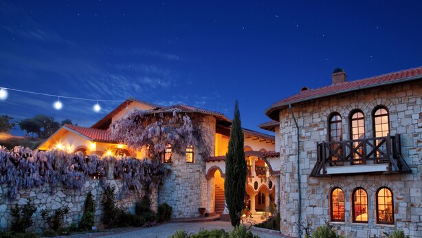 Un edificio de piedra con ventanas arqueadas y un balcón, rodeado de un jardín y luces de cadena.