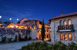 A stone building with arched windows and a balcony, surrounded by a garden and string lights. - Vinifera Vineyards Hotel (Selçuk)