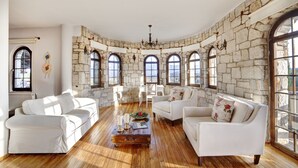 Amplia sala de estar con sofás blancos, una mesa de centro de madera y paredes de piedra.