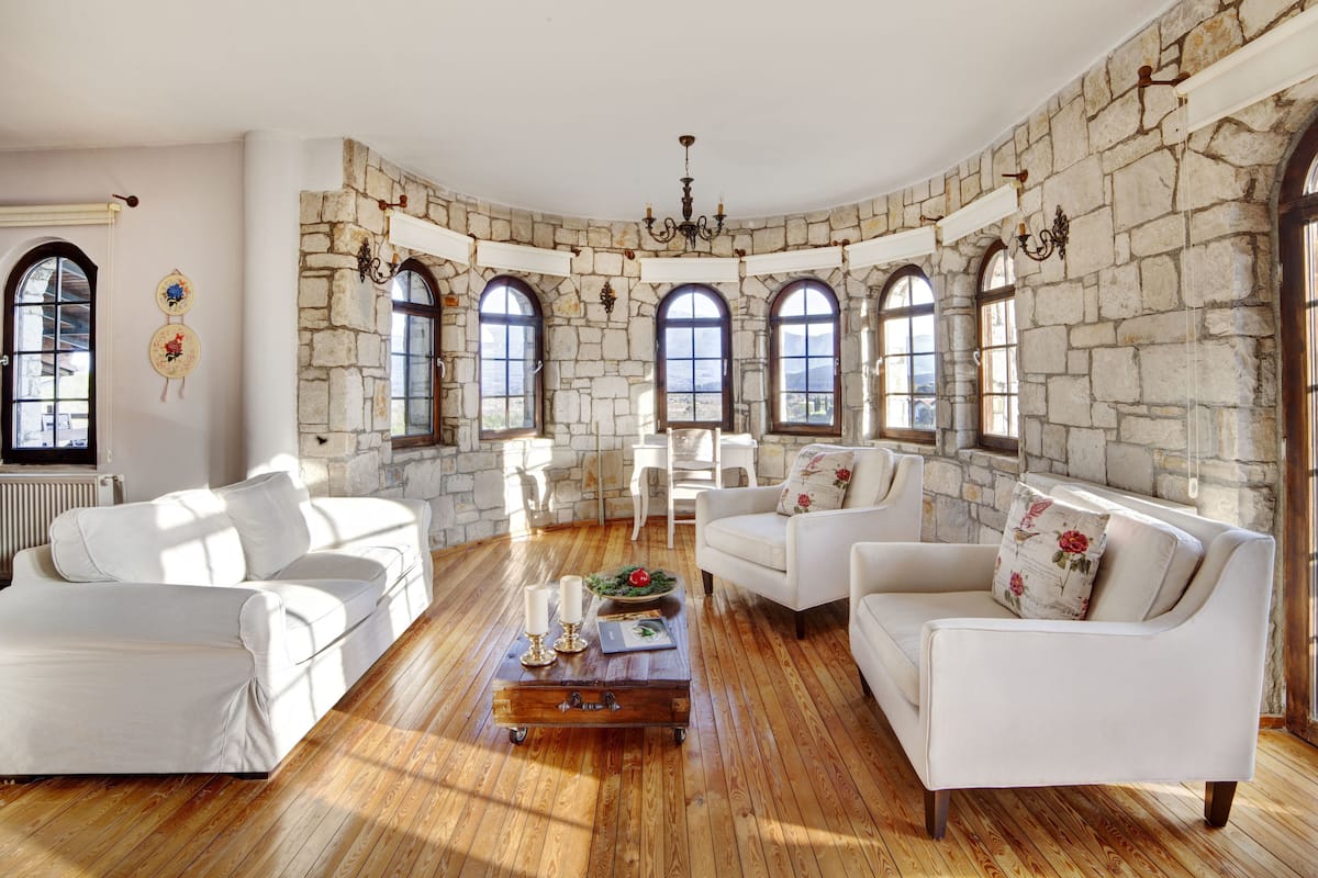A spacious living room with white sofas, a wooden coffee table, and stone walls.