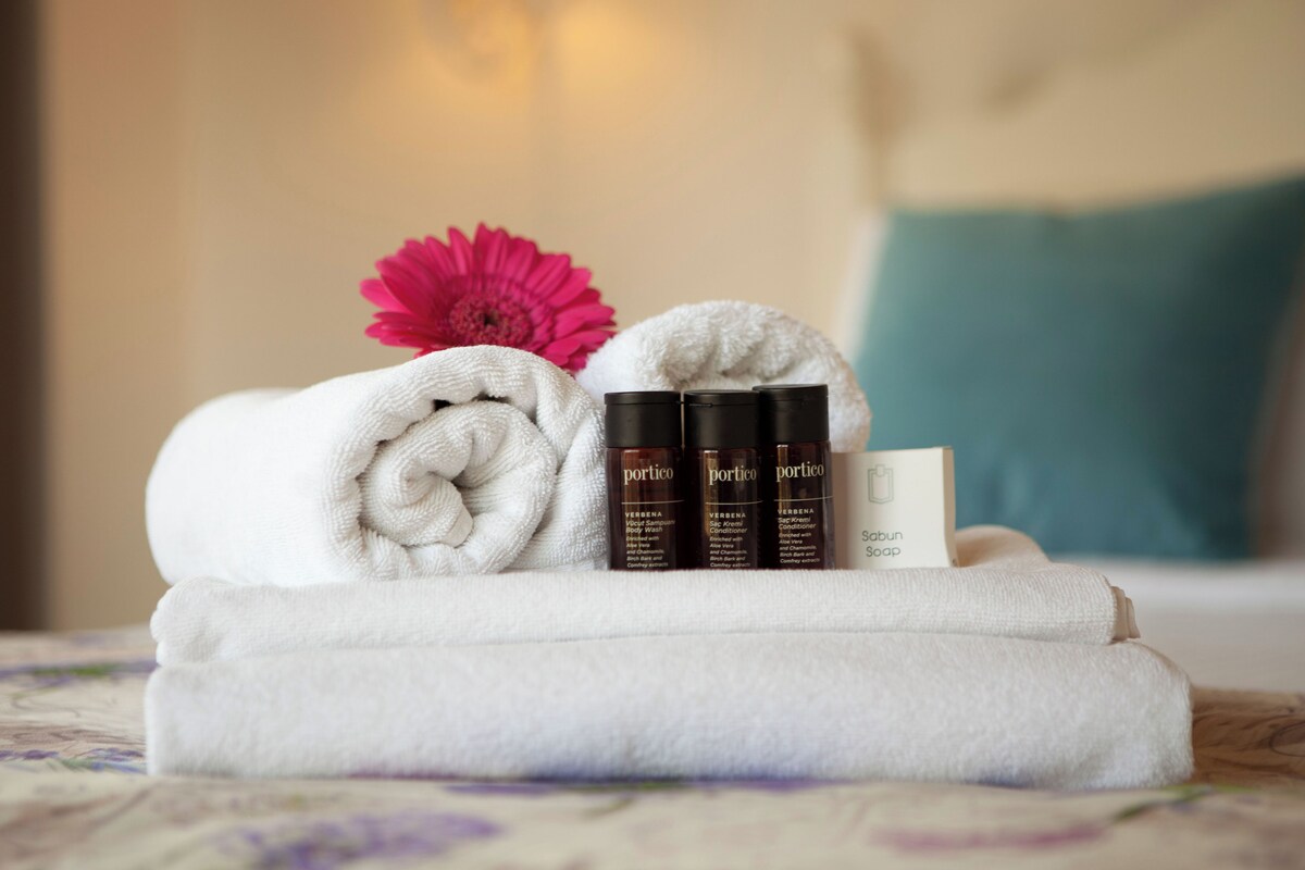 A neatly arranged set of toiletries including a towel, a bottle of shampoo, a bottle of conditioner, and a bar of soap on a bed.