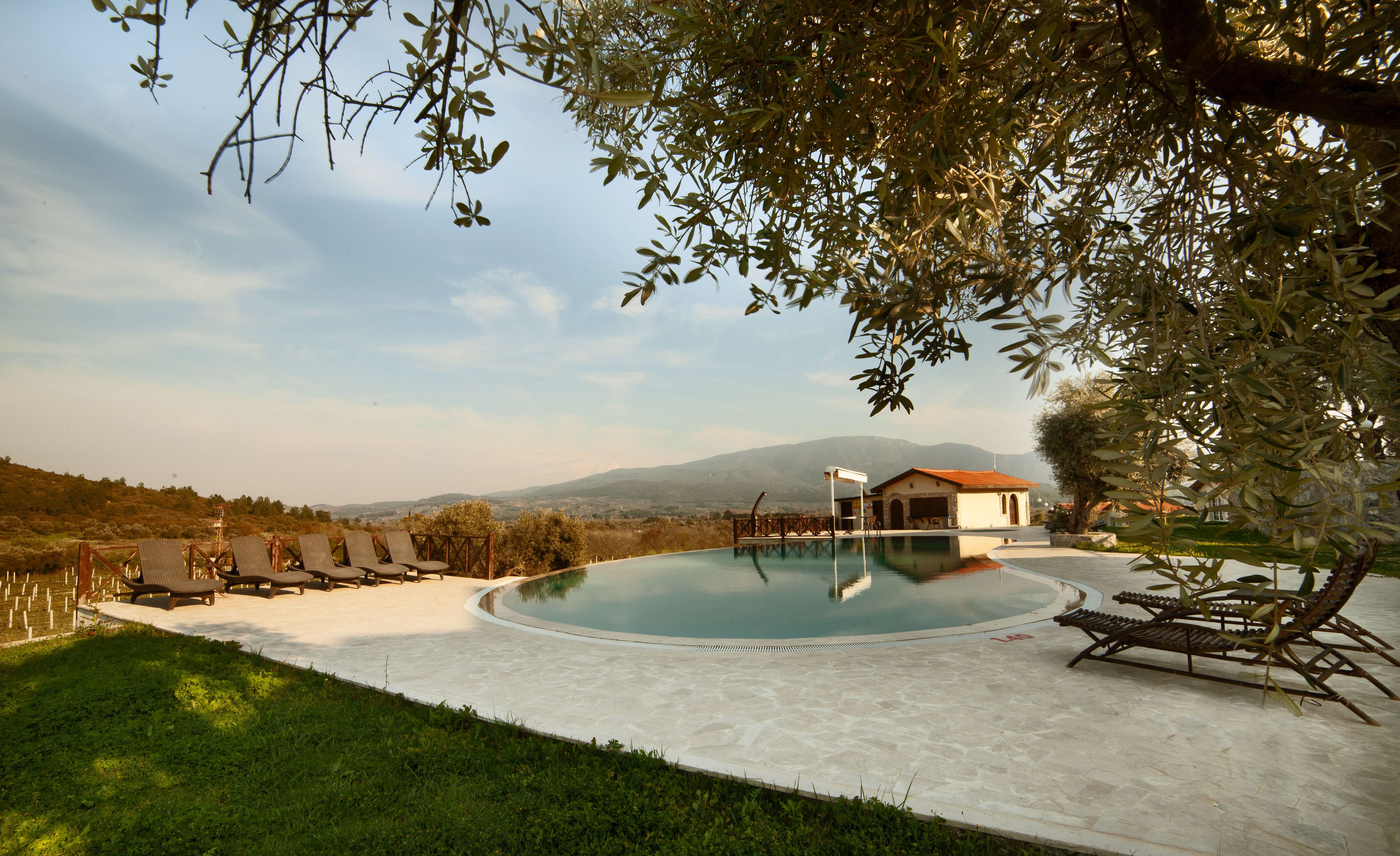 A pool area with lounge chairs, a small building, and a view of mountains.